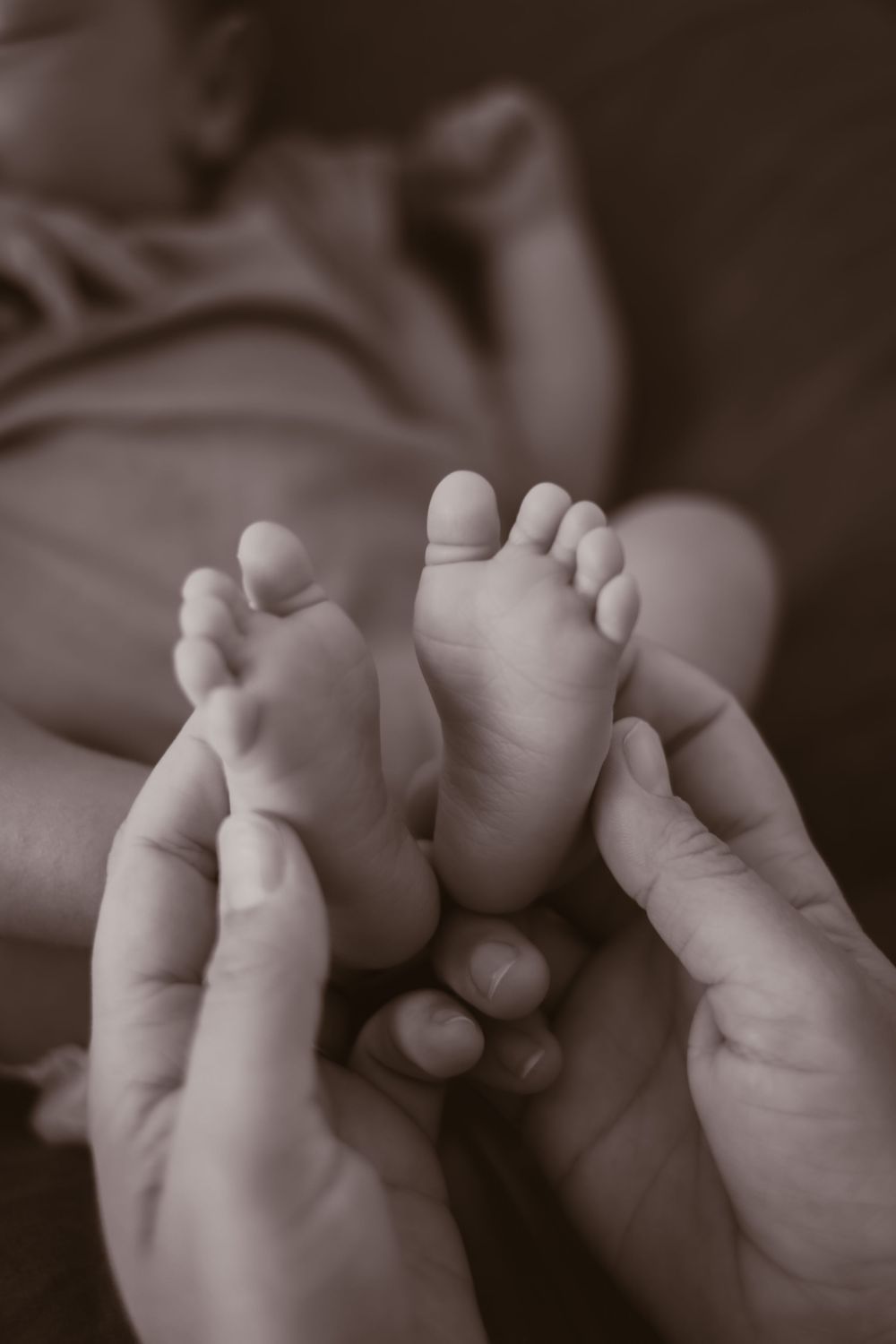 Black and white image of tiny baby feet being held by gentle hands.