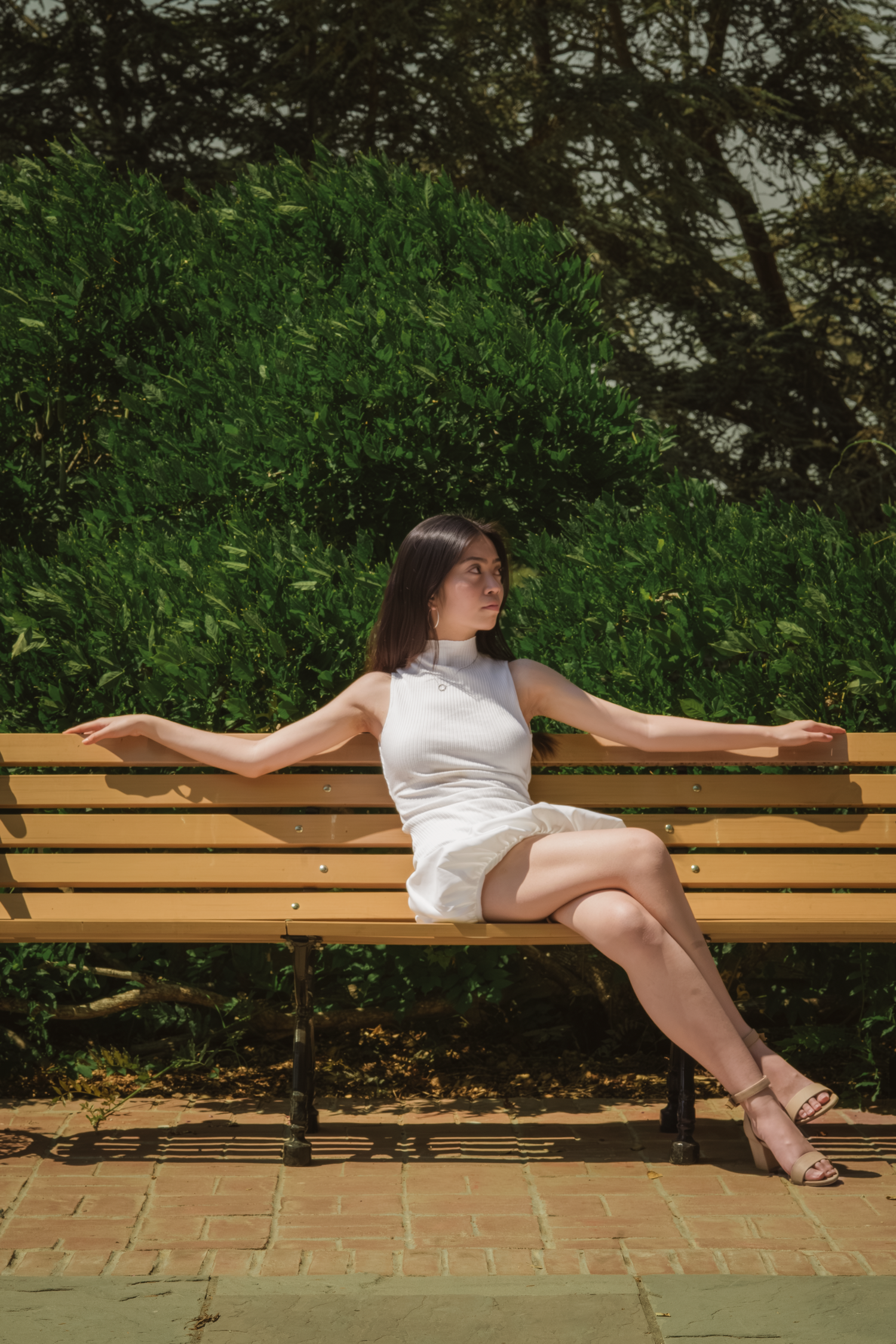 Person in white dress lounging gracefully across wooden park bench in garden setting.