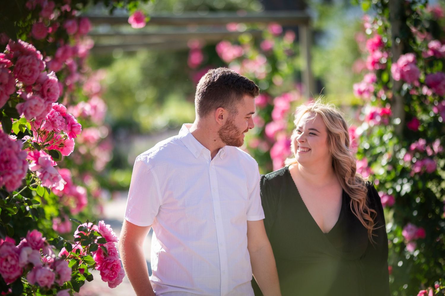 A couple shares a joyful moment in a beautiful garden with blooming pink flowers around them.