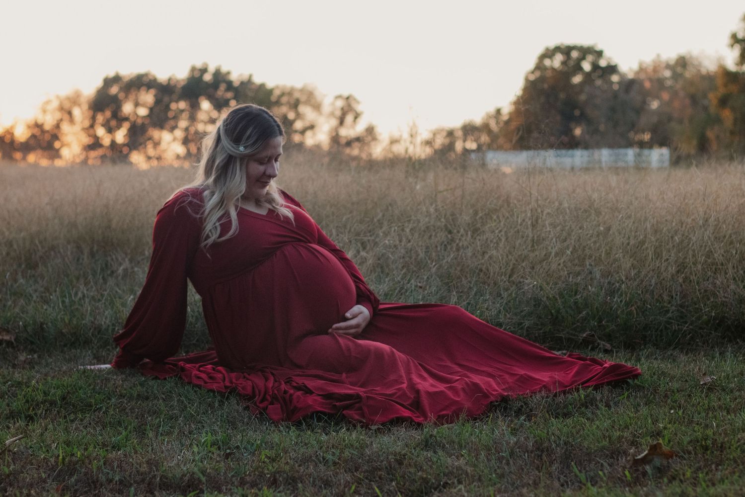Person in flowing burgundy dress lying in golden autumn field at sunset.