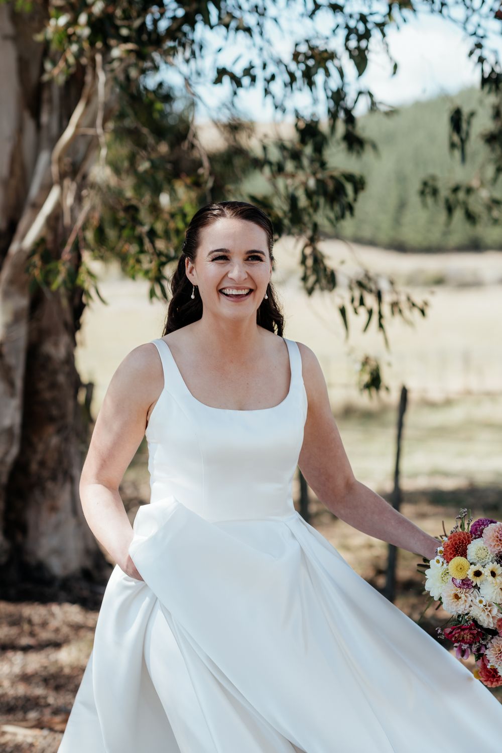 Happy bride in a sleeveless white wedding dress spins joyfully while holding a bouquet at Tironui Farm Martinborough by August and Vine