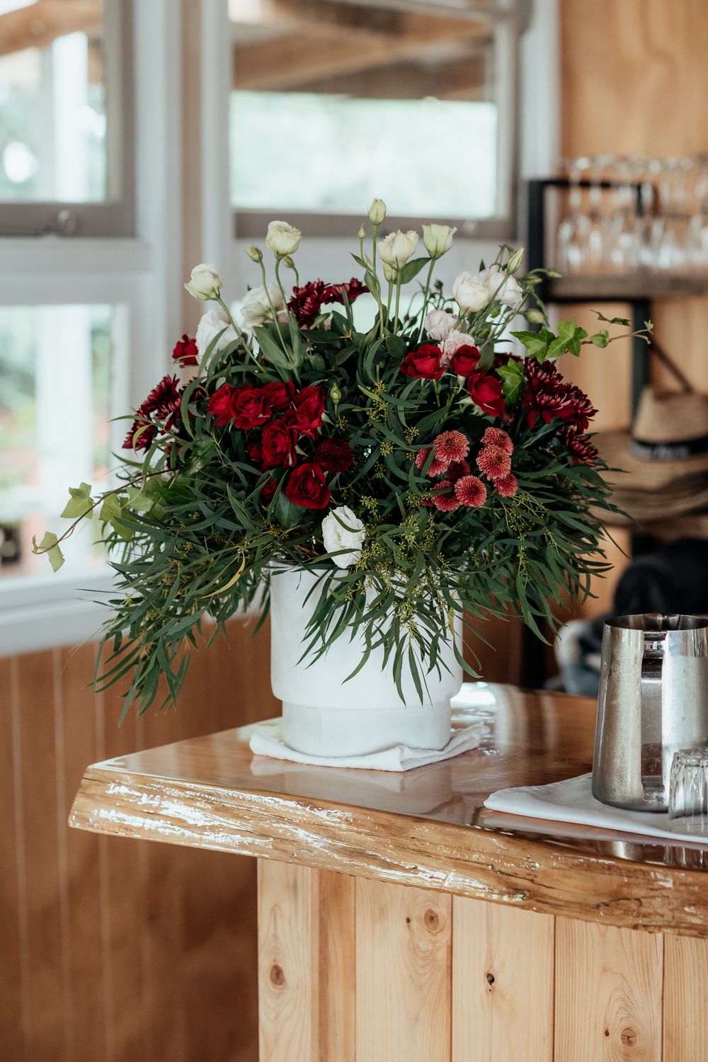 Red floral arrangement in white vase on a wooden bar at Tironui Farm Martinborough by August and Vine