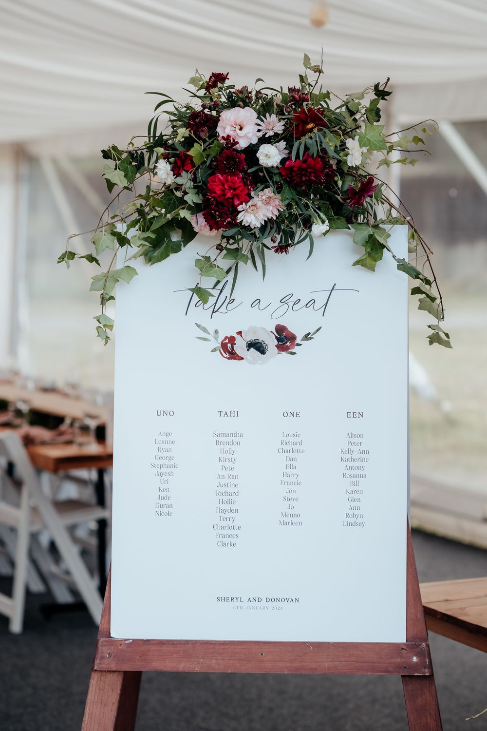 Wedding seating chart decorated with burgundy and white flowers displayed on wooden easel at Tironui Farm Martinborough by August and Vine