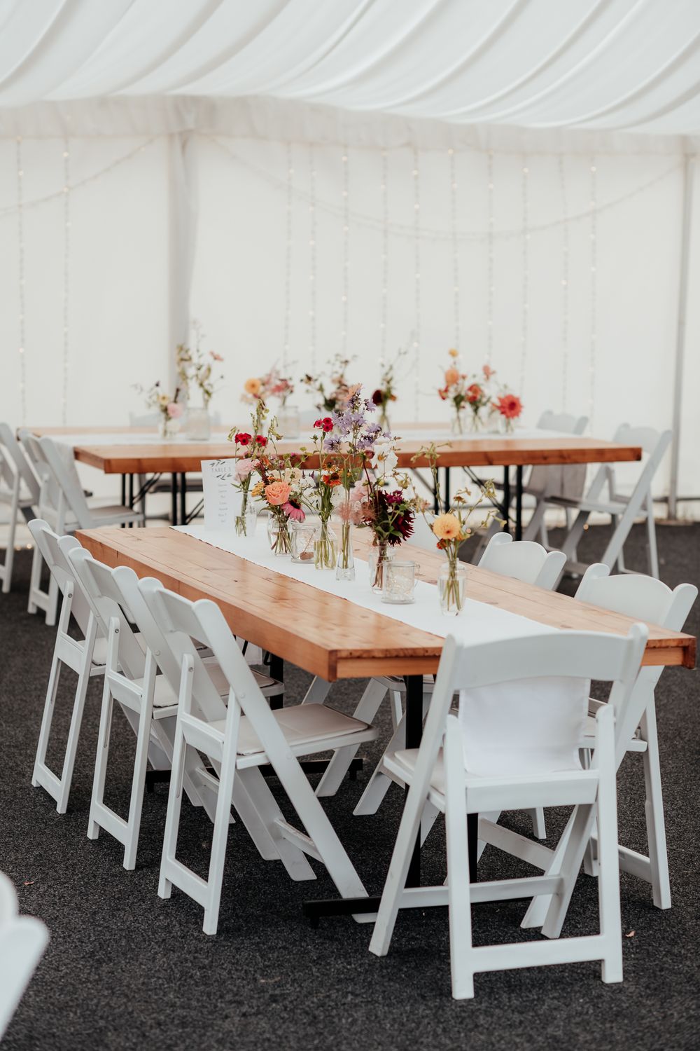 Wooden tables decorated with delicate flowers in vases with white chairs in a marquee at Tironui Farm Martinborough by August and Vine