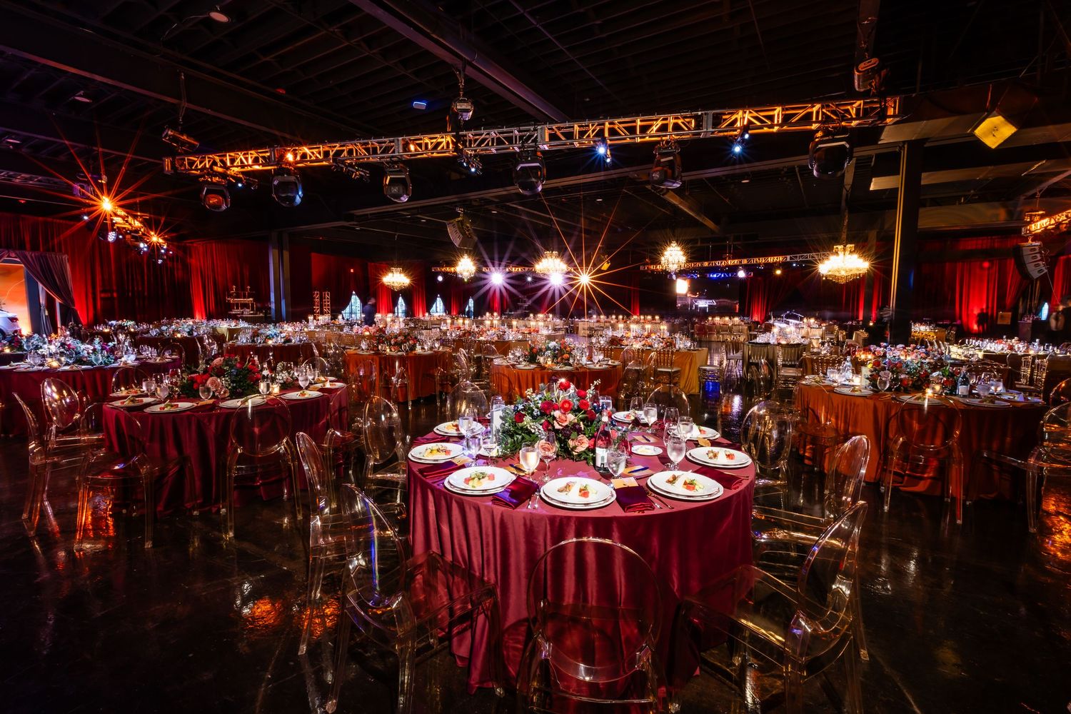Panoramic view of an elegant reception hall setup with round tables and dramatic red lighting for an evening event.