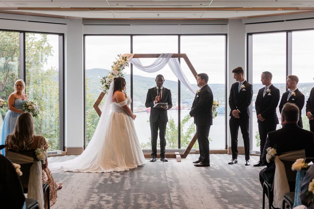 Wedding party stands in line against floor-to-ceiling windows in modern venue.