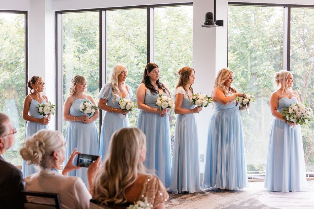 Bridesmaids in light blue dresses gather near large windows creating a beautiful sequence of candid moments.