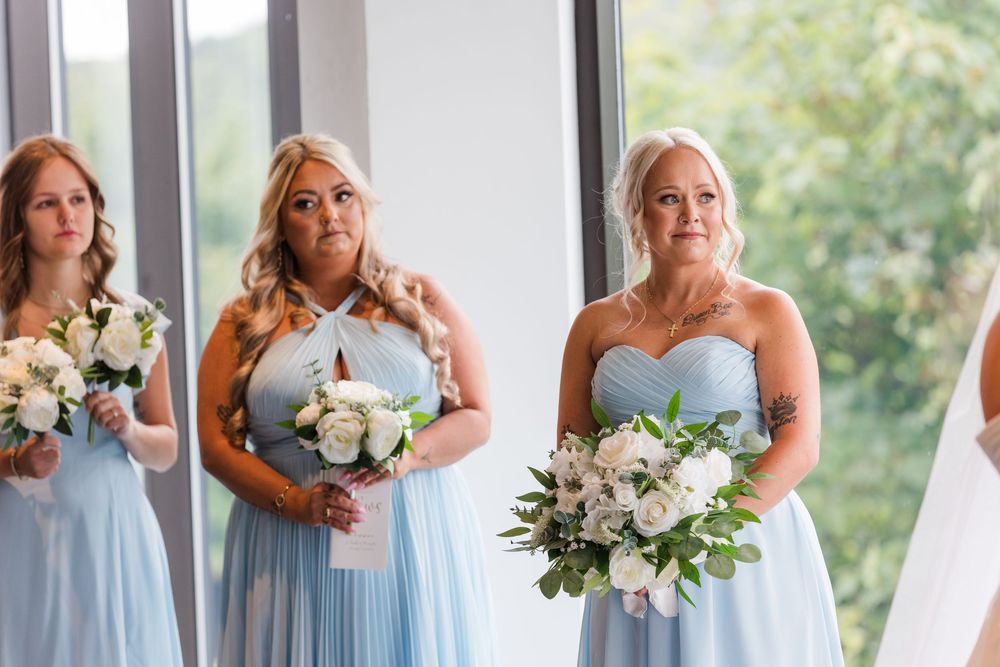 Bridesmaids in light blue dresses hold elegant white floral bouquets during a wedding ceremony.