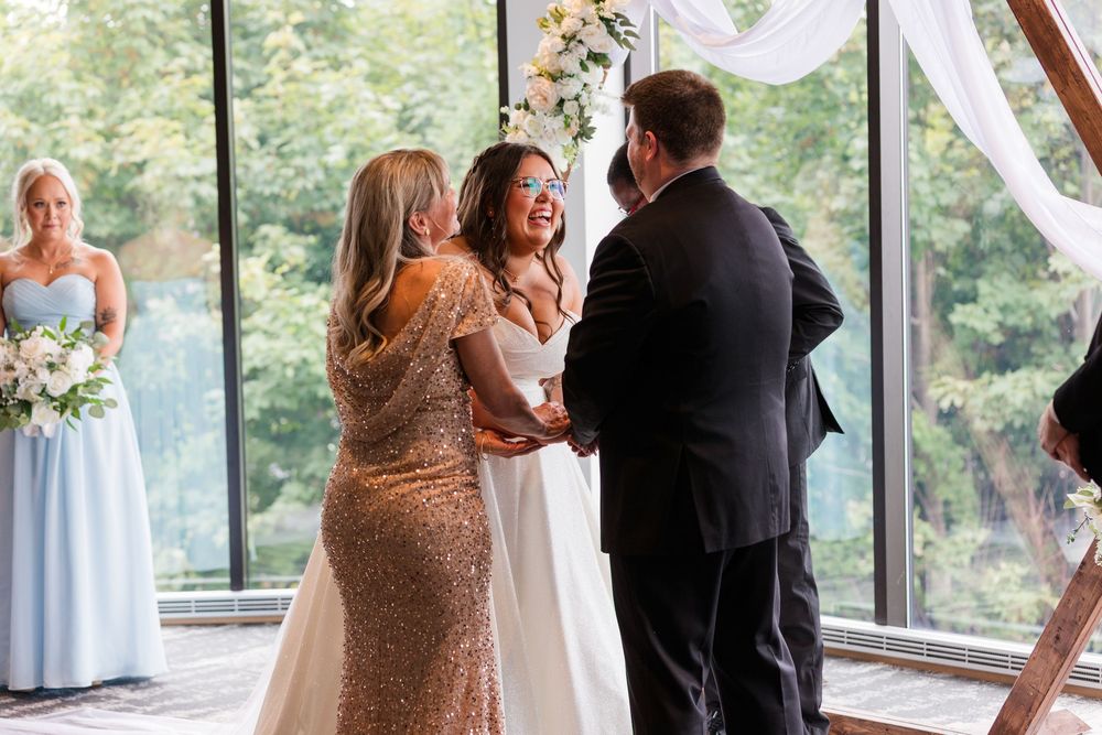 Wedding ceremony guests gathered in a bright sunlit venue with large windows.