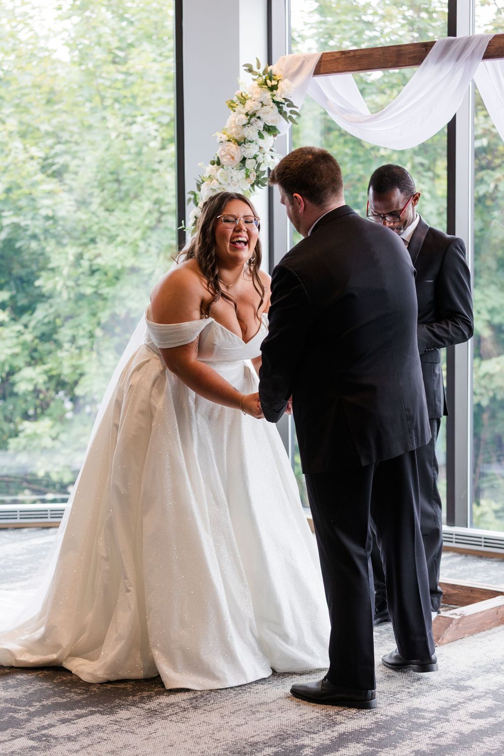 Wedding ceremony participants share joyful moments in a bright windowed venue.