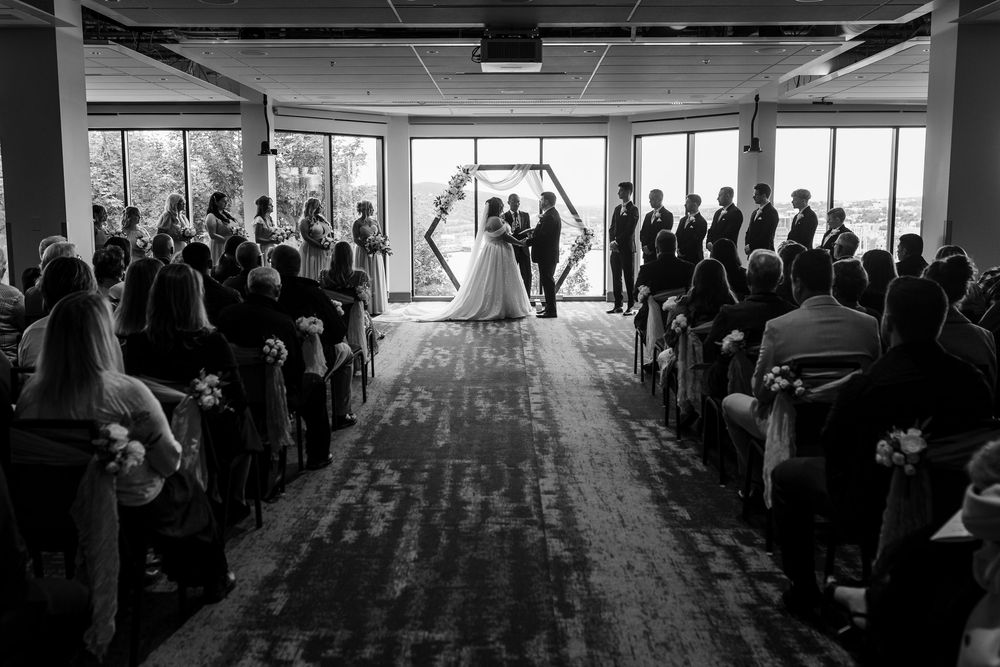 Panoramic view of wedding ceremony attendees gathered in a modern indoor venue with natural lighting.