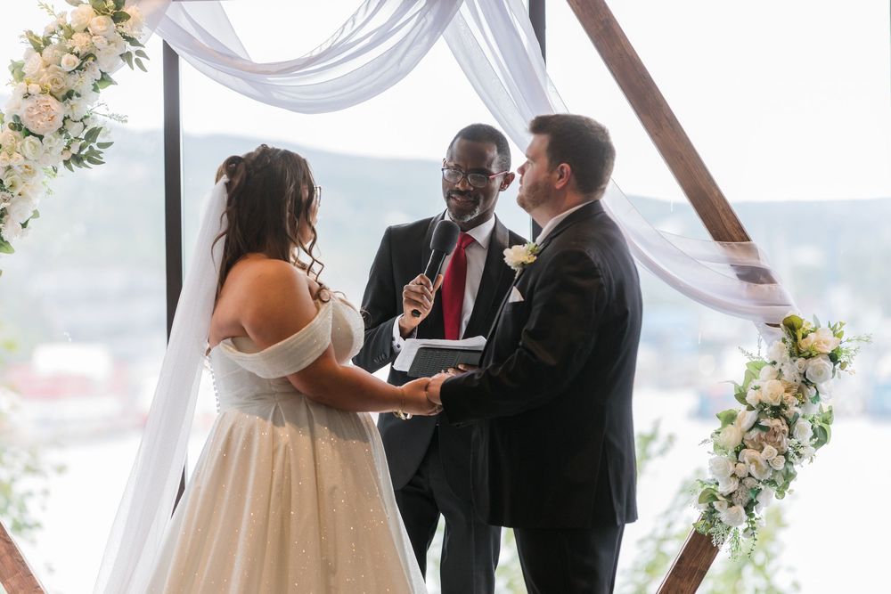Wedding ceremony with white draping and floral arch overlooking scenic waterfront view.