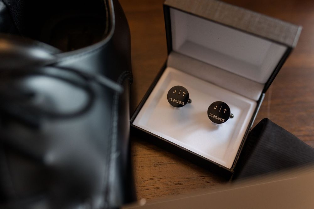 A pair of black vintage style cufflinks displayed in an open white jewelry box on a wooden surface.