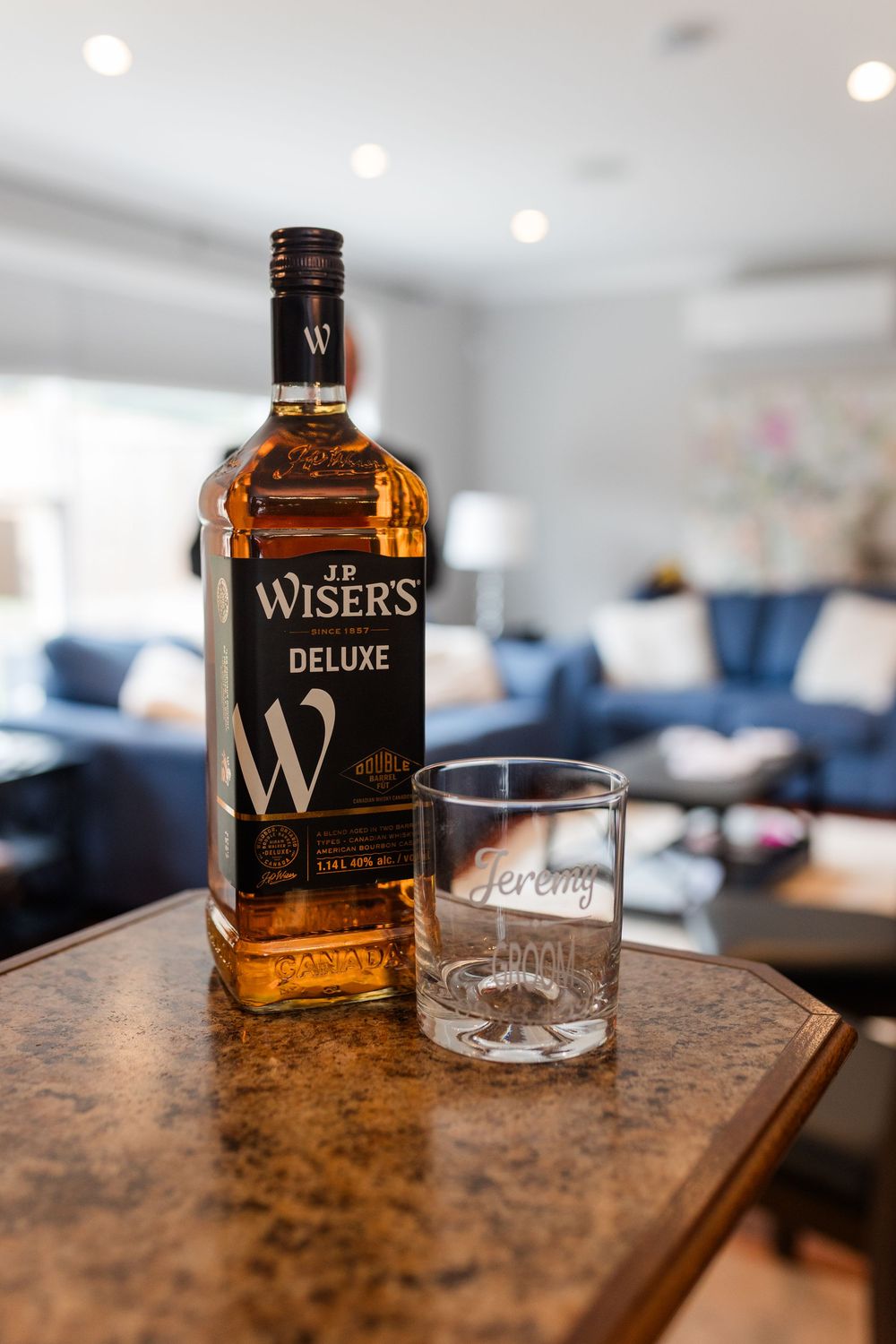 A bottle of Wiser's deluxe Canadian whisky sits next to an empty glass on a wooden surface in a modern interior.
