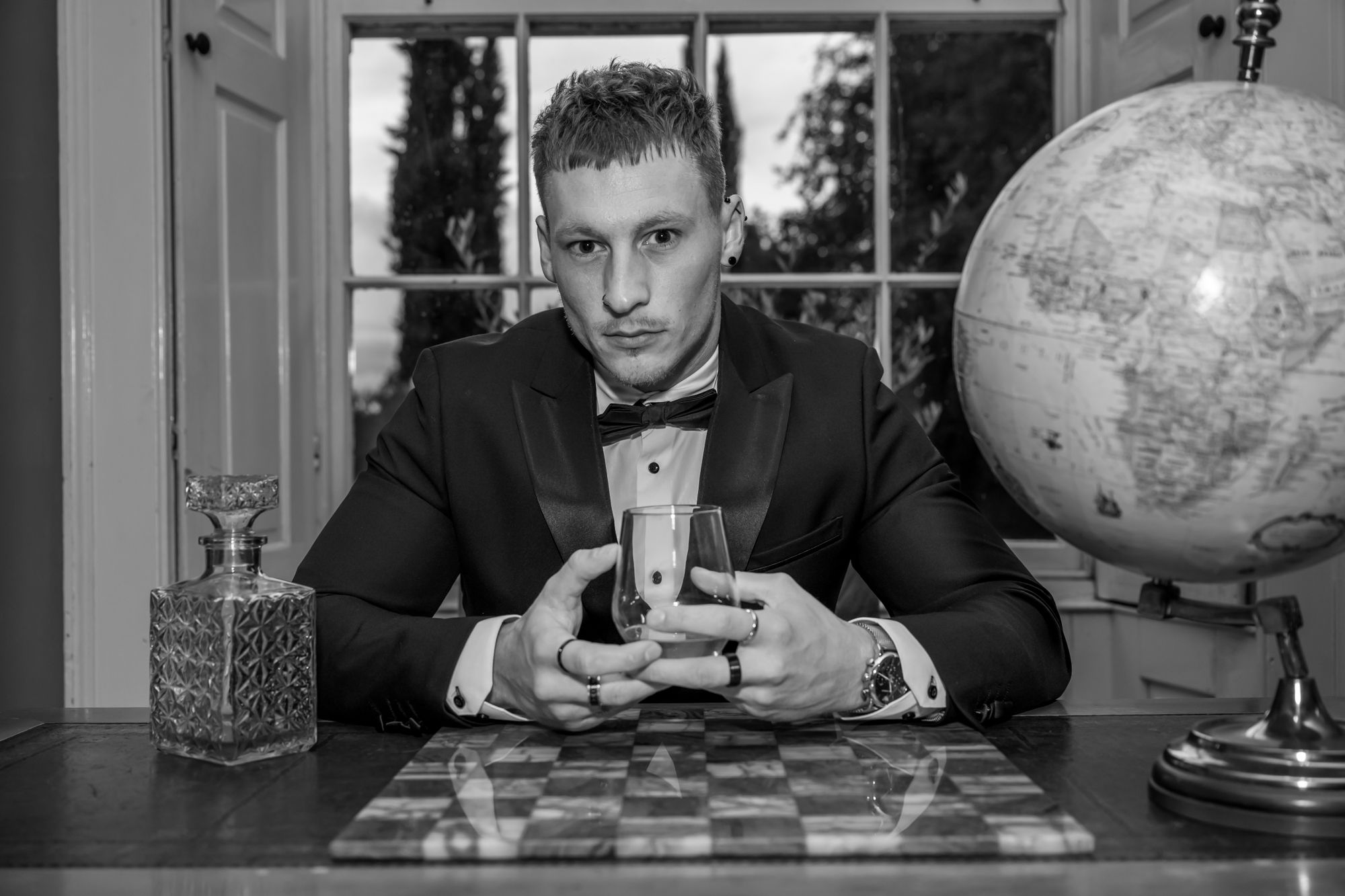 A series of black and white photos showing someone playing chess and contemplating moves at a table with a globe nearby.