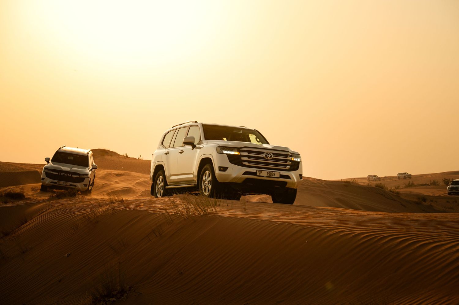 Seven off-road vehicles traverse sandy desert dunes during a golden sunset in United Arab Emirates.