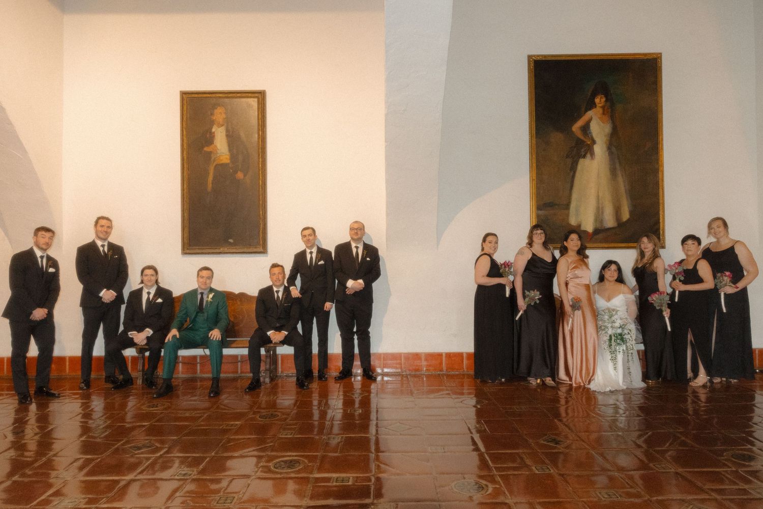 A panoramic view of people standing in formal attire along the walls of an art gallery with paintings displayed.
