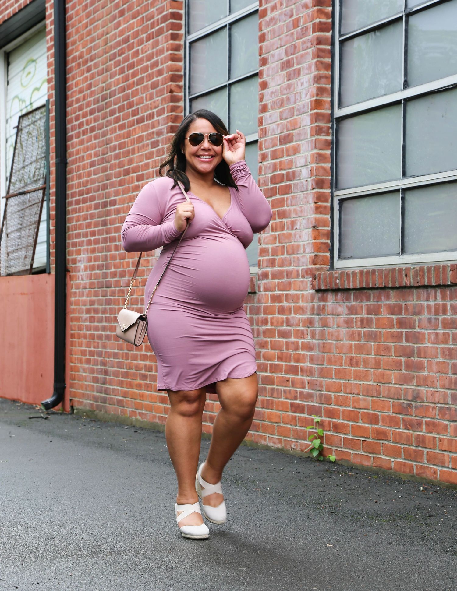 Woman in pink sweater dress and white shoes poses playfully against brick wall in four sequential shots.