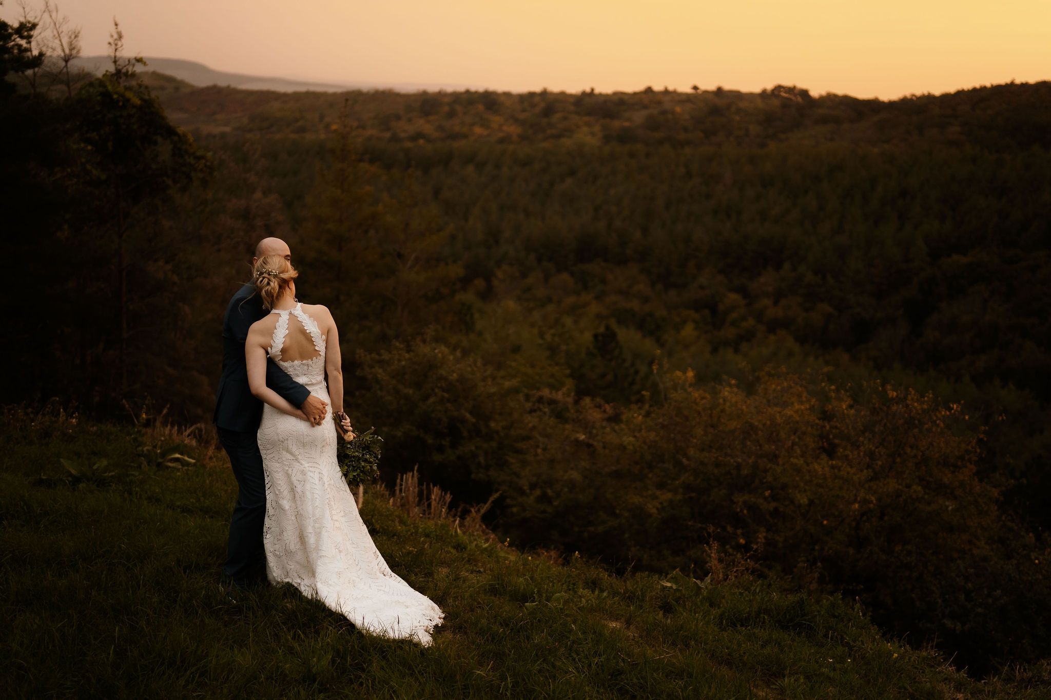A romantic sunset wedding portrait overlooking a vast valley landscape.