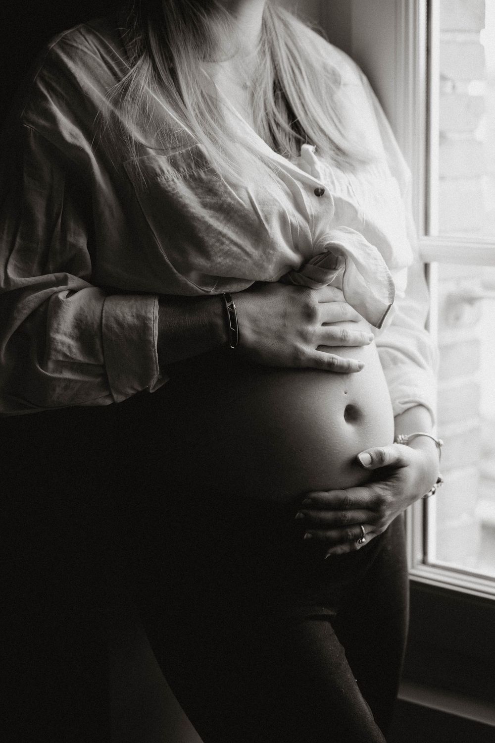 Black and white maternity photo series showing a pregnant belly silhouetted against a window in dramatic lighting.
