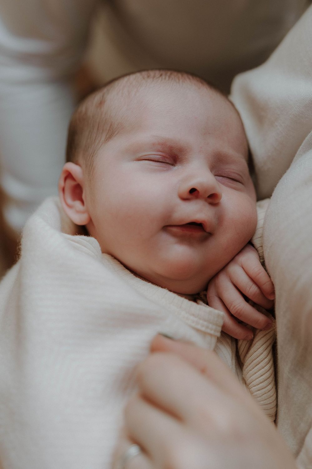 A peaceful sleeping newborn baby wrapped in soft beige blankets smiles contentedly.