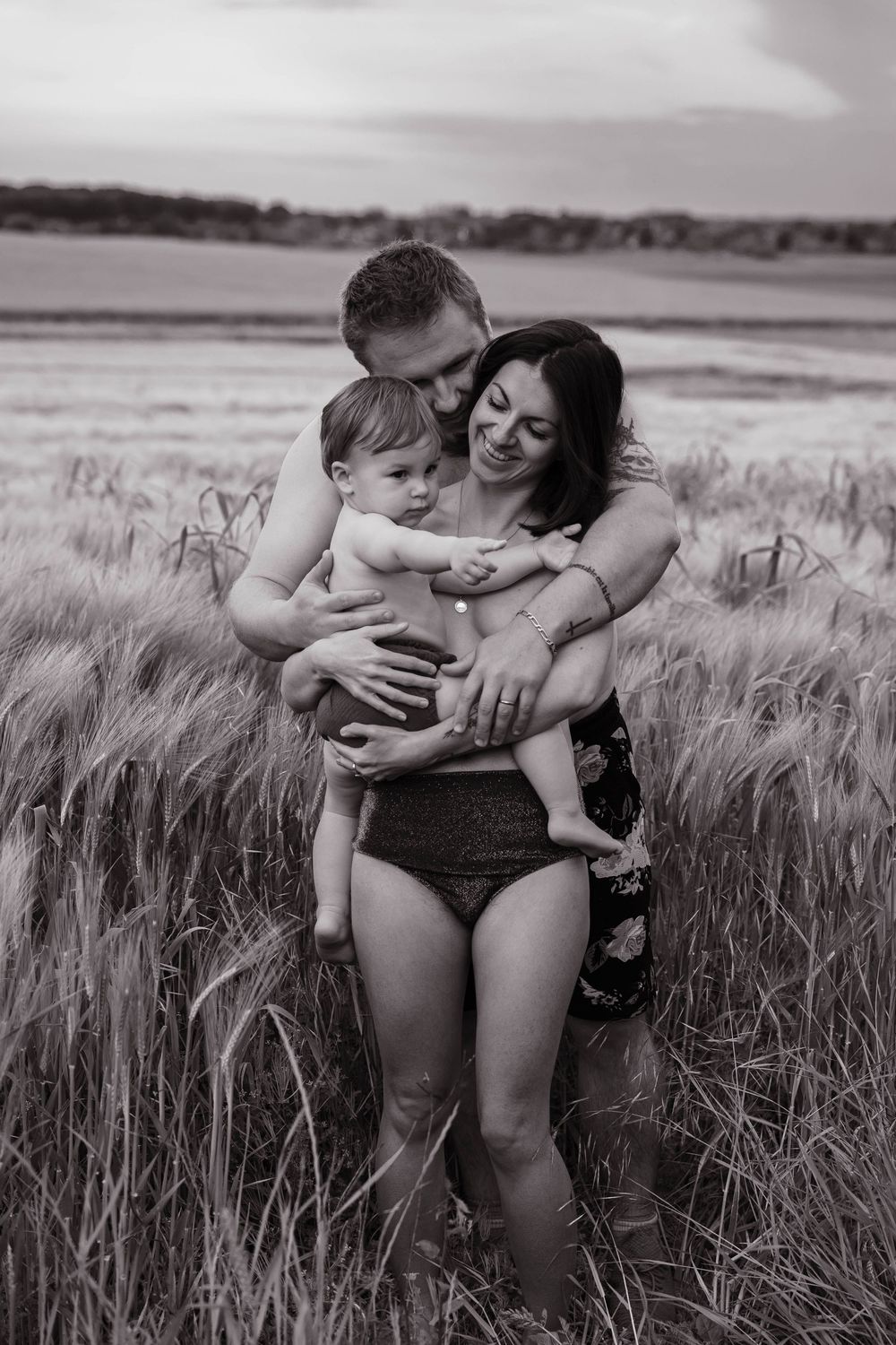 A family shares tender moments together while sitting in a rustic wheat field in black and white photographs.