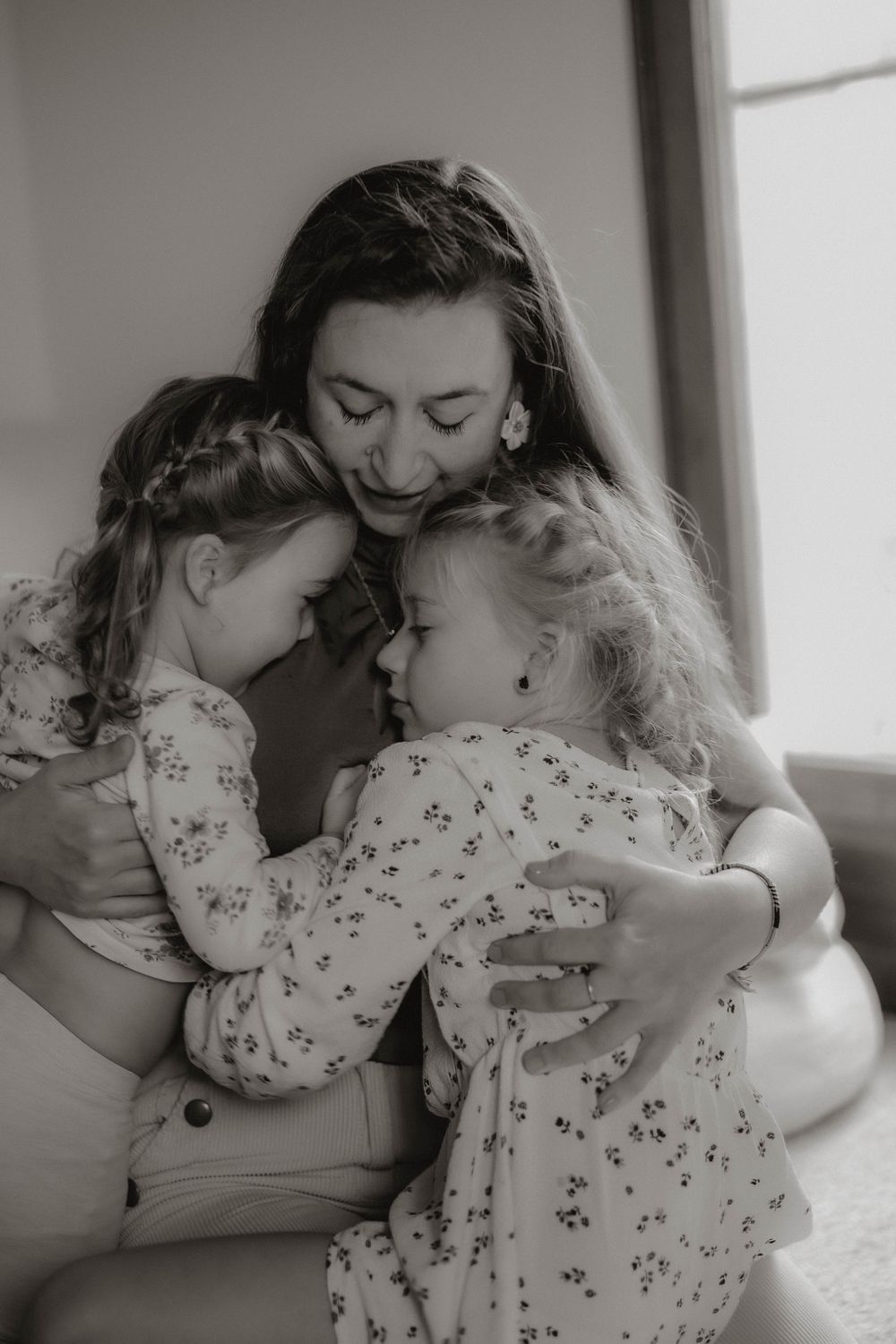 Black and white photo series showing tender moments between a parent and child in soft window light.