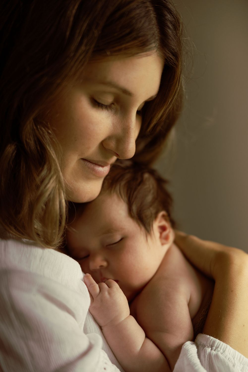 Tender moment of a smiling mother cradling her sleeping newborn baby in warm light.