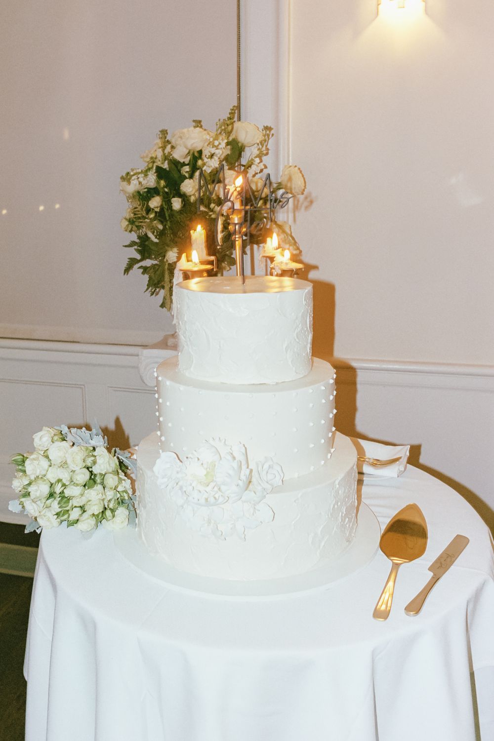 Elegant white tiered wedding cake decorated with floral details and gold accents.