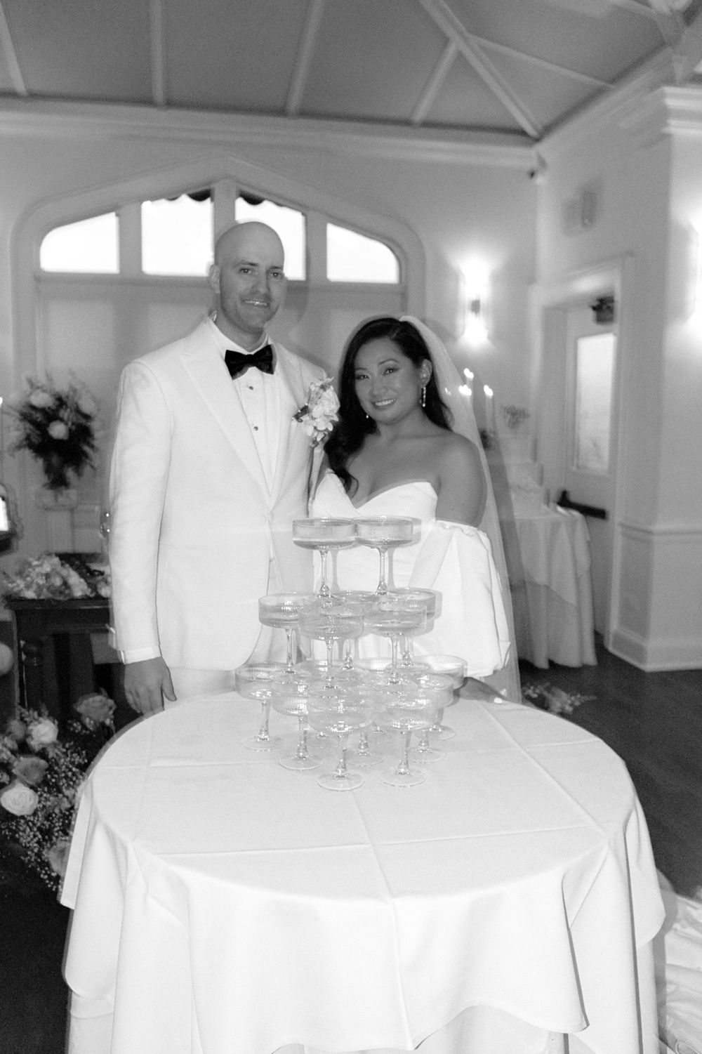 Wedding reception setup with champagne tower and white tablecloths in an elegant white room.
