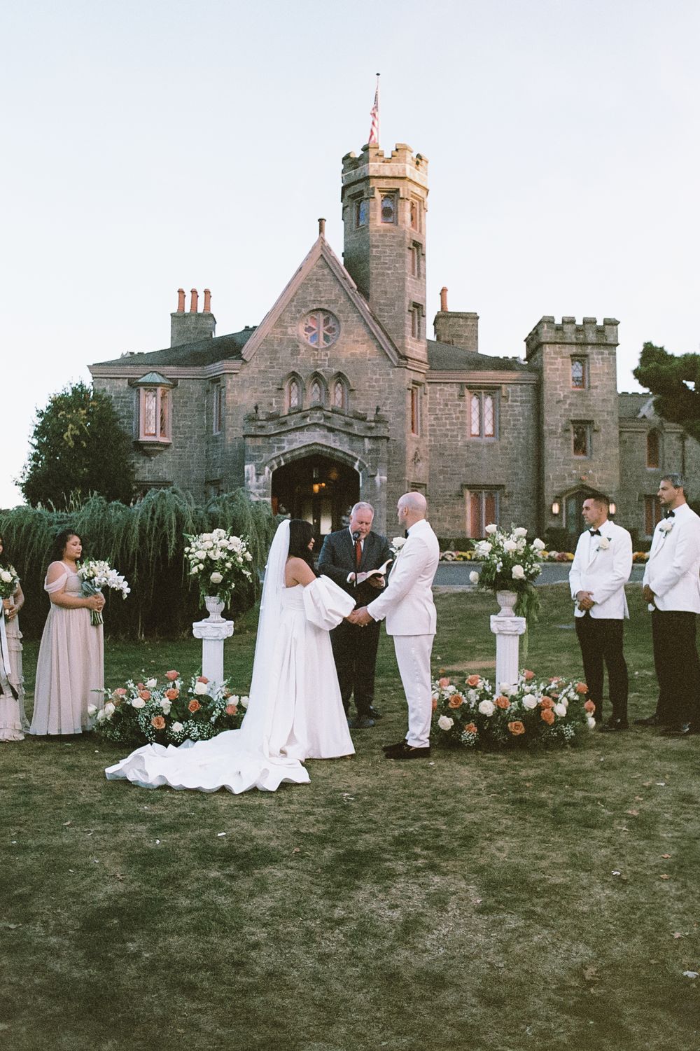 Wedding ceremony taking place on the lawn of a Gothic stone castle.