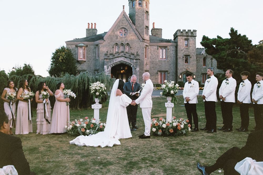 Wedding party gathered on the grounds of a historic stone castle at dusk.