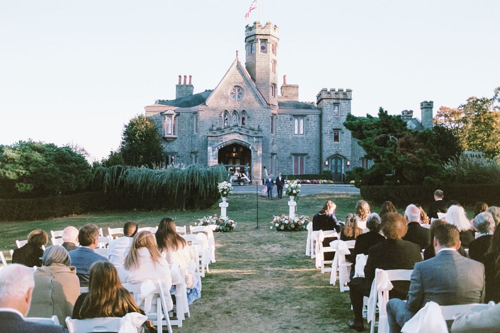 Wedding ceremony setup with white chairs facing stone castle-like building.