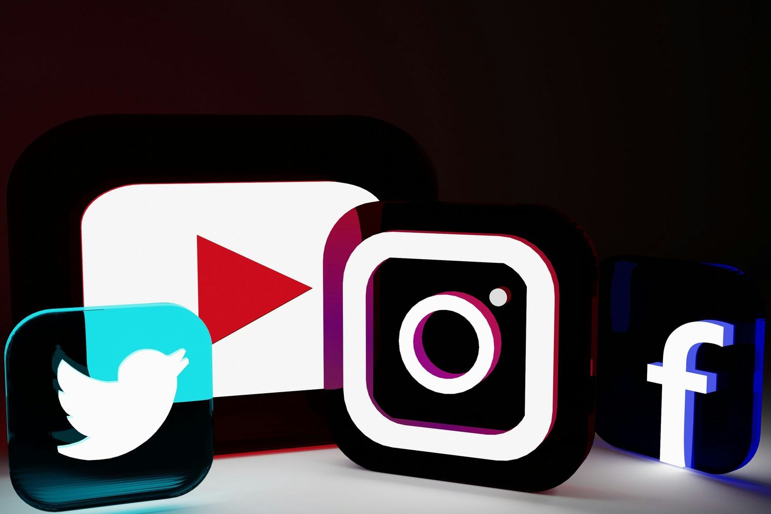 Illuminated social media logos for Twitter, YouTube, Instagram and Facebook against dark background.