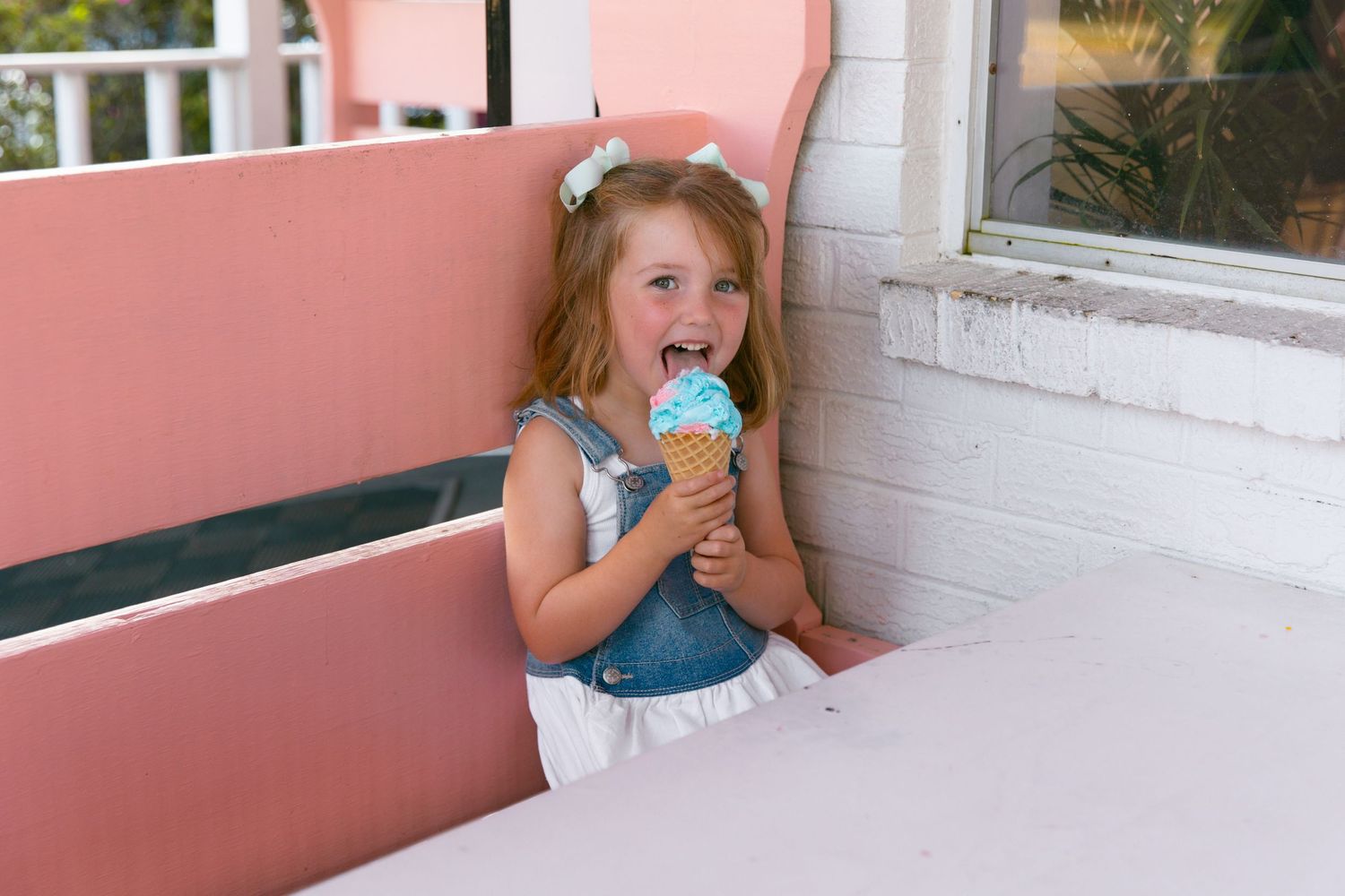 Young child enjoying blue ice cream cone while seated at outdoor table.
