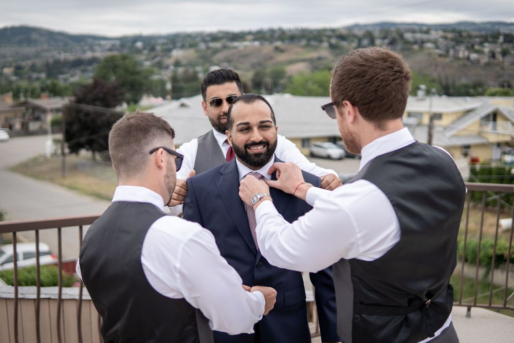 Groomsmen help adjust a tie during wedding preparations on an outdoor terrace.