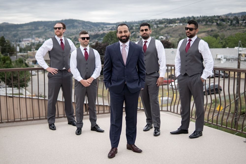 A groom and his groomsmen pose confidently on a terrace overlooking a hillside landscape.