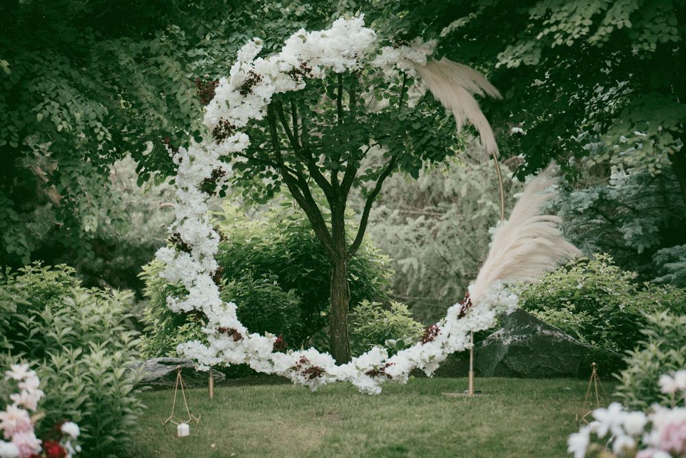 A white floral arch creates an elegant circular frame against a natural forest backdrop.