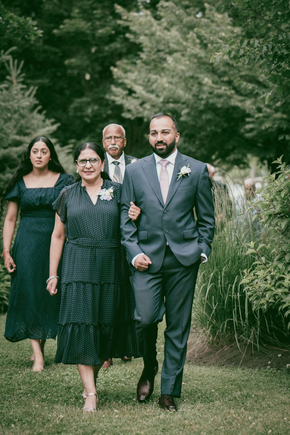 Small wedding party walks along a garden path during formal portraits.