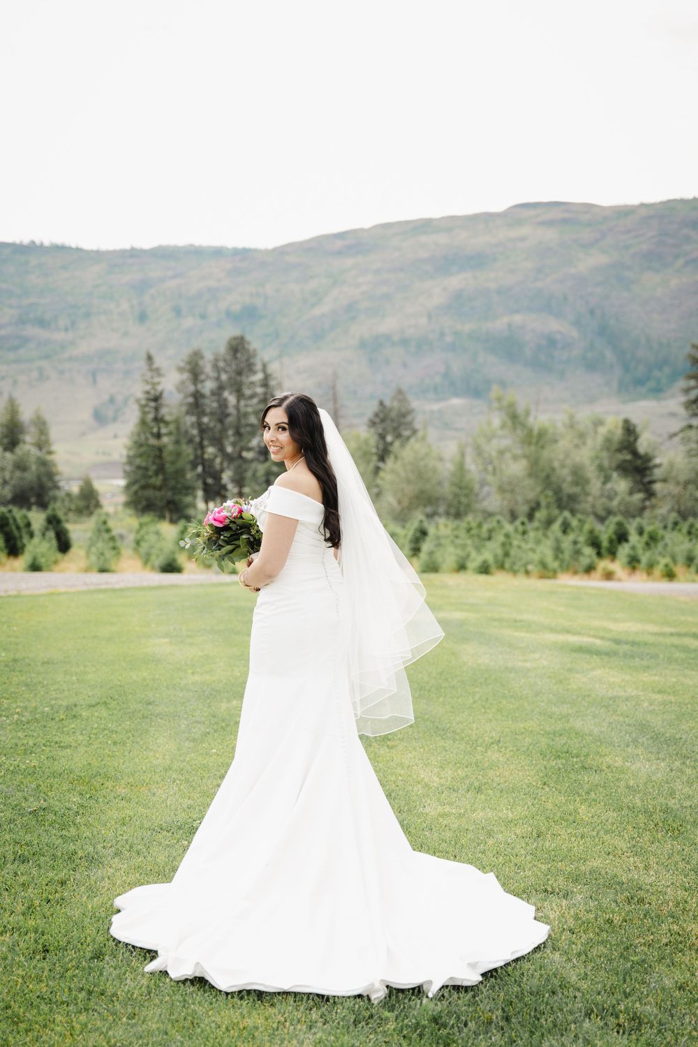A bride in a classic white mermaid gown poses against mountain scenery.