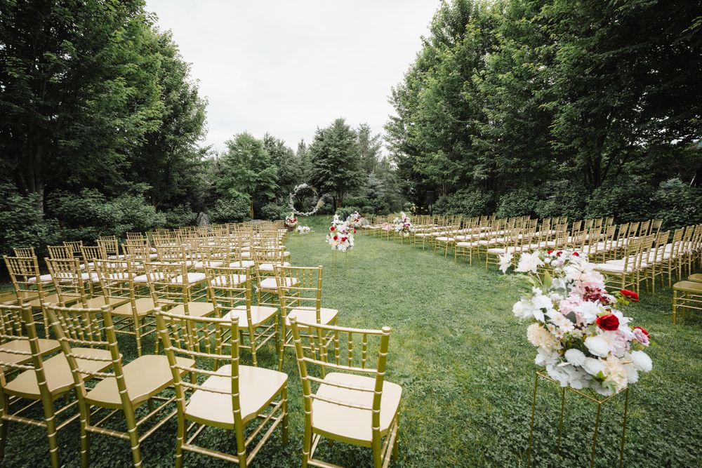 An outdoor wedding venue setup with gold chairs and floral decorations on a manicured lawn.