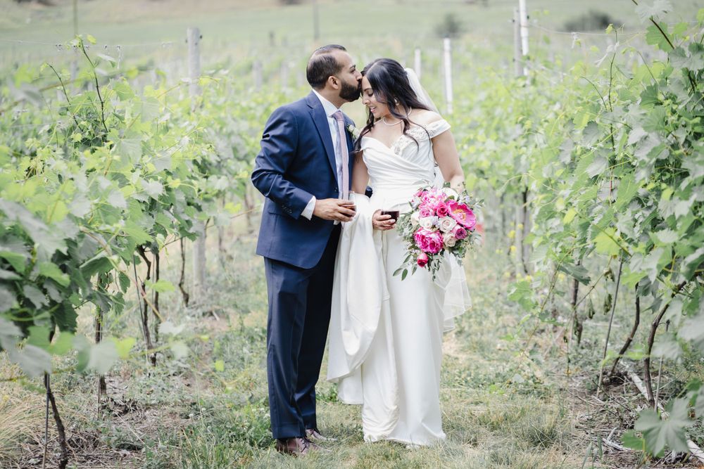 Romantic wedding portrait of couple among vineyard rows with pink bouquet.
