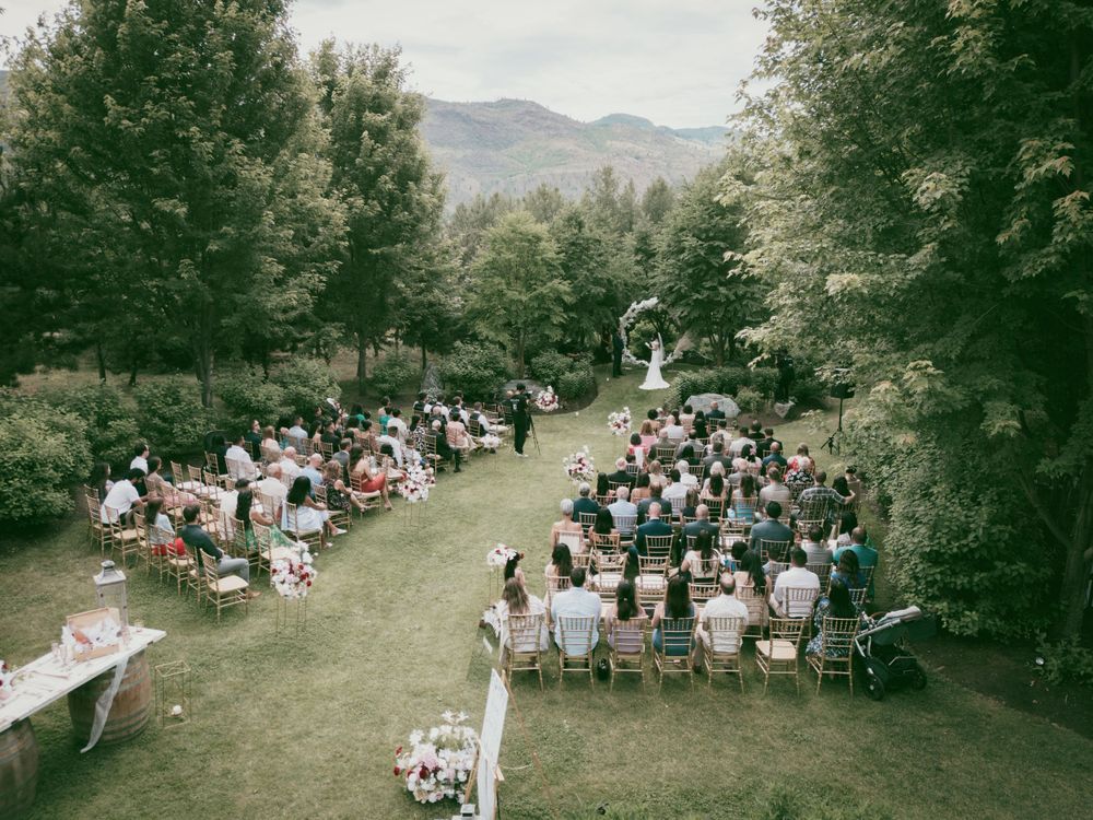 Aerial view of outdoor wedding ceremony with guests seated in white chairs surrounded by mountain landscape.