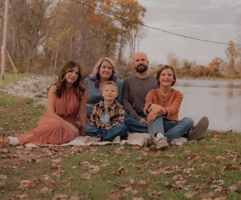 Family group sitting together by lake during autumn season.