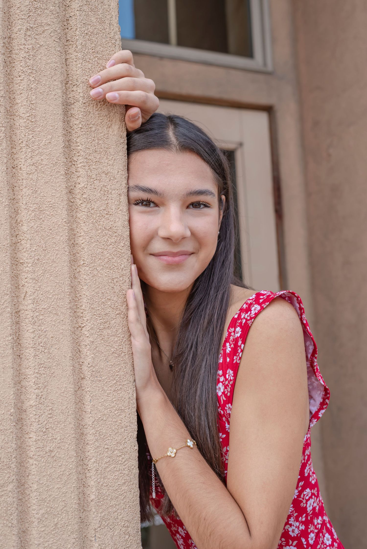 A candid portrait pose against a textured stucco wall in warm sunlight.