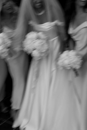 Motion-blurred black and white photo of bridesmaids in white dresses holding bouquets.