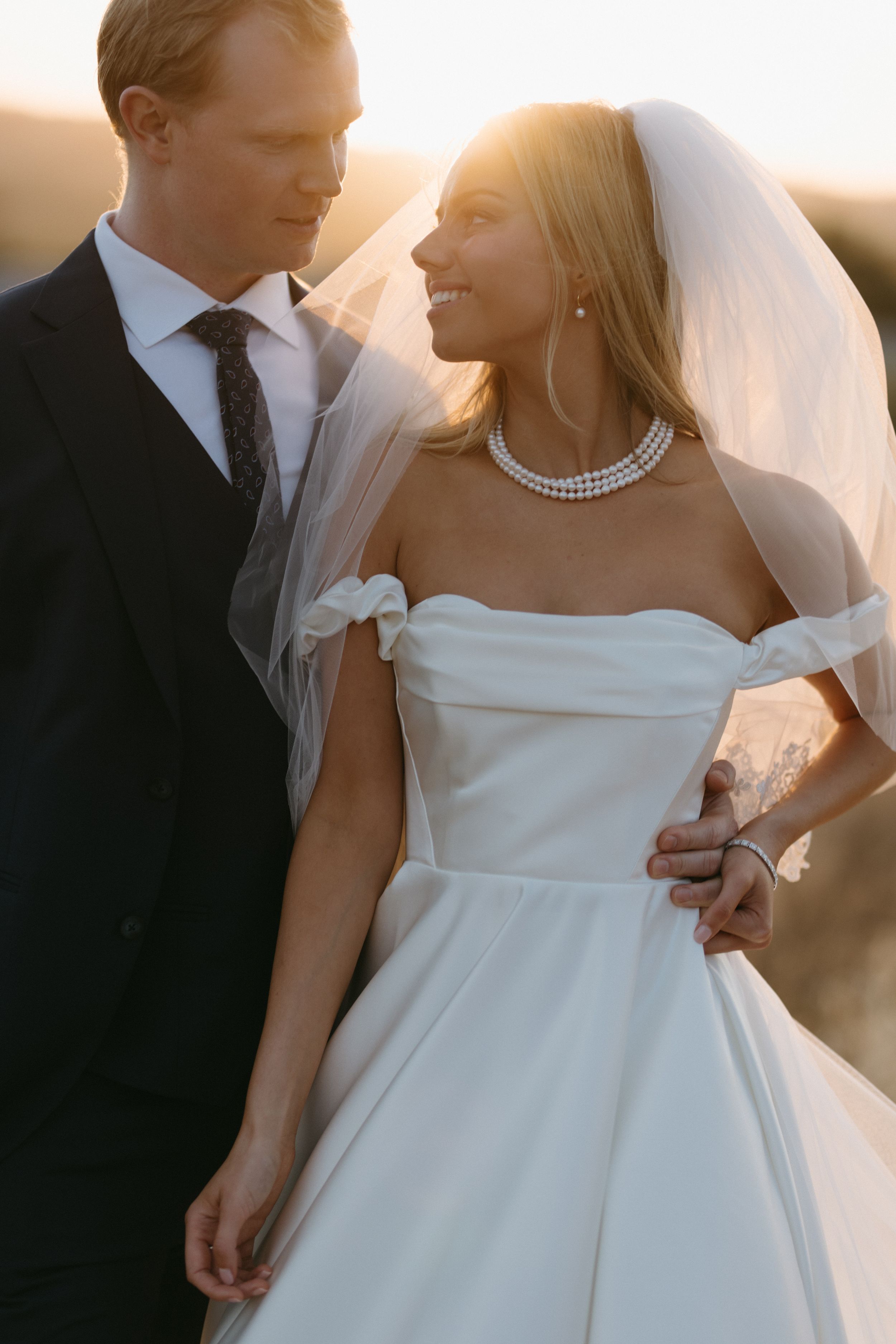 Intimate sunset portrait of newlyweds with bride wearing pearl necklace and classic white gown.