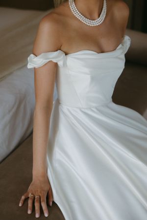 Close-up detail of off-shoulder wedding dress bodice with pearl necklace and flowing skirt.
