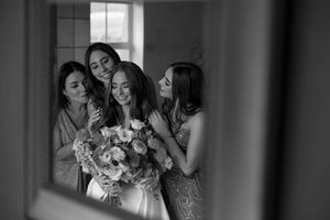 Black and white photo of bridesmaids sharing joyful moments by a window.