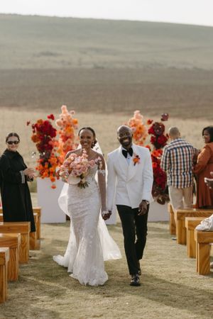 Wedding ceremony aisle decorated with vibrant red and orange florals against rolling hills landscape.